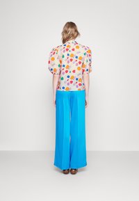 Kleurrijke blouse met bloemenpatroon en pofmouwen, gecombineerd met wijde blauwe broeken. Lichtgewicht stof, heldere kleuren en een relaxte pasvorm.