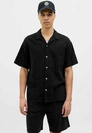 Chemise noire à manches courtes, à boutons, en tissu texturé, associée à un short assorti, avec des boutons blancs et un col.