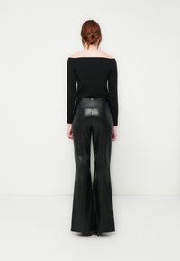 Top nero off-the-shoulder a maniche lunghe abbinato a pantaloni in pelle nera a vita alta e svasati, con un dettaglio dorato sul retro.