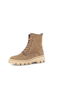 Bottines en cuir suédé marron avec bout rond, fermeture à lacets à l'avant, et semelle en caoutchouc beige épaisse avec de profondes rainures et une languette à l'arrière.