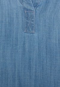 Ljusblå denimtyg som har en kort V-ringning med förstärkt sömnad. Texturen är slät med subtila färgvariationer.