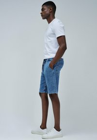 Pantalones cortos de mezclilla en azul claro con dos bolsillos laterales, cintura con cordón y un ajuste estándar, combinados con una camiseta de algodón blanca lisa y zapatillas blancas.