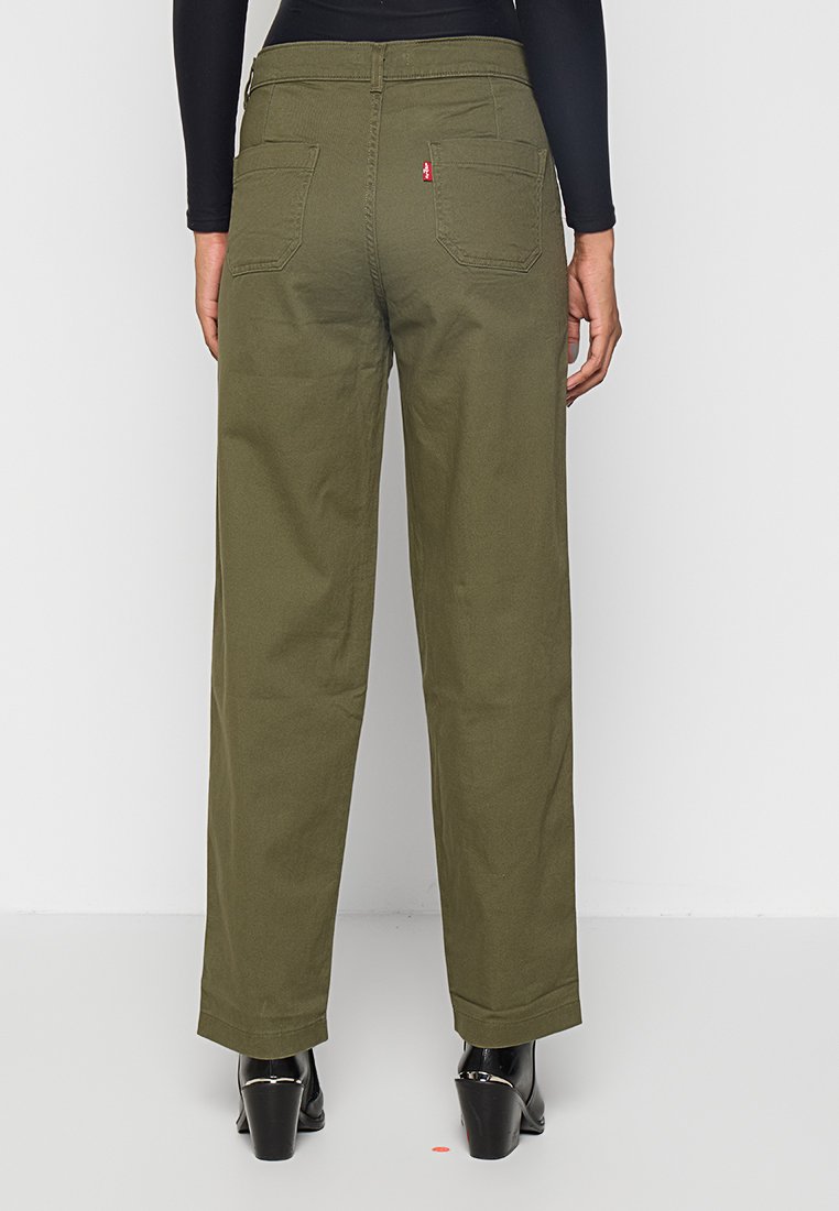 Pantalons larges en vert olive en coton, avec des poches arrière et une petite étiquette rouge au niveau de la taille. Tissu texturé avec une finition mate.