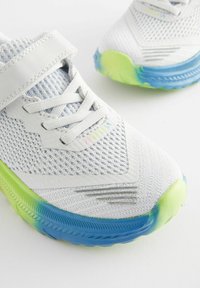 Lekkie buty sportowe z białą siateczkową cholewką, szarymi skórzanymi akcentami i designem podeszwy w gradientzie od niebieskiego do zielonego.