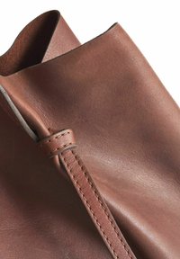 Bruine leren tas met een gladde textuur, gekenmerkt door een gestikte zijkant en een gevouwen rand, met een rijke, warme tint.