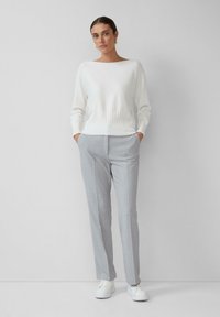 Pull en tricot blanc avec une texture côtelée, associé à un pantalon taillé gris clair et des baskets blanches. Design minimaliste, coupe décontractée.