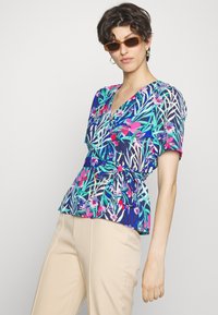 Blusa de mangas curtas com estampa floral, decote em V profundo, cintura peplum e detalhes com laço. As cores incluem azul marinho, verde, rosa e branco.