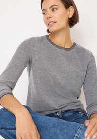 Graues, strukturiertes Langarmshirt mit rundem Halsausschnitt und gerippten Bündchen, kombiniert mit blauen Jeans.