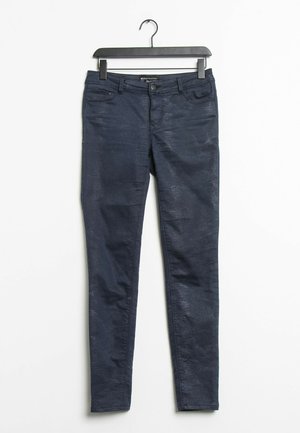 Jeans ajustados de corte slim en azul oscuro, confeccionados en denim con un patrón texturizado sutil. Diseño de cinco bolsillos con cierre frontal de botón y cremallera.