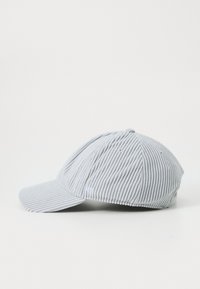 Una gorra de pana de color gris claro con visera curvada, que presenta detalles de costura sutiles y un pequeño logo en la parte frontal, situada contra un fondo blanco.