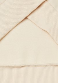 Světlý béžový materiál s kontrastní žebrovanou strukturou. Disponuje hladkou, jemnou vnitřní vrstvou. Viditelné švy podél lemování.
