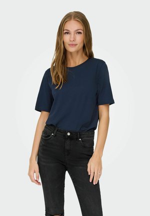 T-shirt blu navy a maniche corte realizzato in tessuto liscio, abbinato a jeans neri a vita alta con ginocchia strappate e dettagli in bottone argentato.