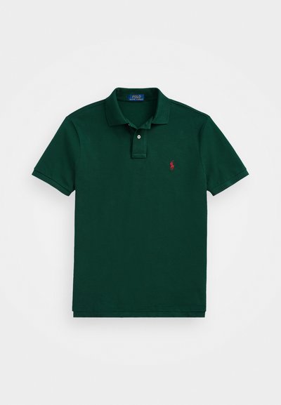 Tumši zaļš polo krekls, kas izgatavots no kokvilnas, ar klasisku apkakli, diviem pogām un mazu sarkanu logotipu kreisajā krūtī.