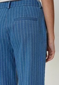Modre prugaste kavbojke s slim fit krojem, z zadnjim žepom, lahkotno teksturo in krojenim pasom. Vertikalne bele pruge.