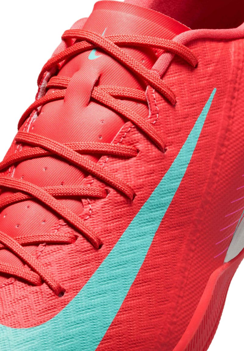 Czerwony but sportowy z fakturowaną cholewką, z turkusowym logo Nike, wyraźnymi sznurowadłami i amortyzowaną podeszwą.