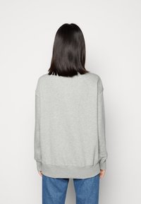 Grå sweatshirt med avslappnad passform, sänkt axel och ribbade muddarna. Slät yta, rund halsringning och en något längre bakre fåll.