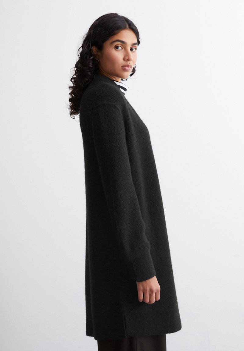 Langer schwarzer Pullover aus weichem, strukturiertem Stoff. Verfügt über einen lässigen Schnitt mit langen Ärmeln und einem geraden Saum, der bis zur Mitte des Oberschenkels reicht.