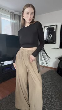 Juodas ilgomis rankovėmis viršus su frill detalėmis, derinamas su smėlio spalvos platėjančiomis kelnėmis, turinčiomis lygią tekstūrą ir aukštu liemeniu.