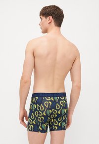 Men's underwear featuring a navy base with a colorful avocado pattern. The elastic waistband displays "BJÖRN BORG" branding.