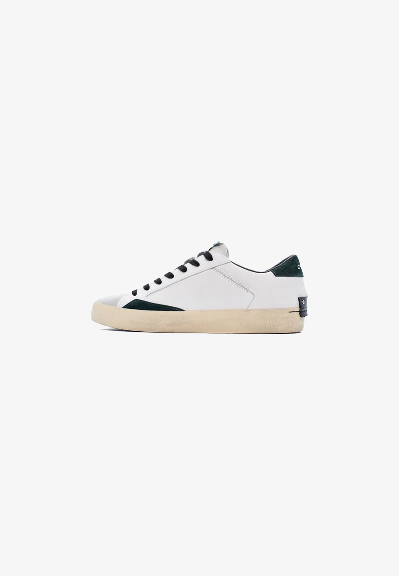 Sneaker bianca con tomaia in pelle liscia, dettagli verde scuro sul tallone e sul lato, occhielli neri e suola in gomma beige textured.