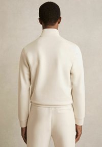 Hanorac bej cu manșete și guler cu nervuri, textură netedă, combinat cu pantaloni asortați, văzut din spate.