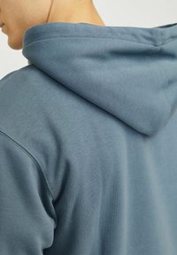 Hoodie in een gedempt blauwe kleur, gemaakt van zachte stof. Heeft een stikseldetail langs de schouder en een ontspannen pasvorm ontwerp.