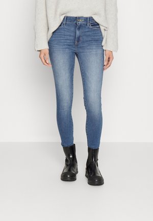 Jeans ajustados en denim azul desgastado, con una cintura alta y un sutil efecto de desgaste. Combinados con botas negras de altura hasta el tobillo.