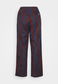 Calças largas com riscas verticais vermelhas e azuis, feitas de algodão. Apresentam padrões gráficos pretos e dois bolsos traseiros. Textura suave.