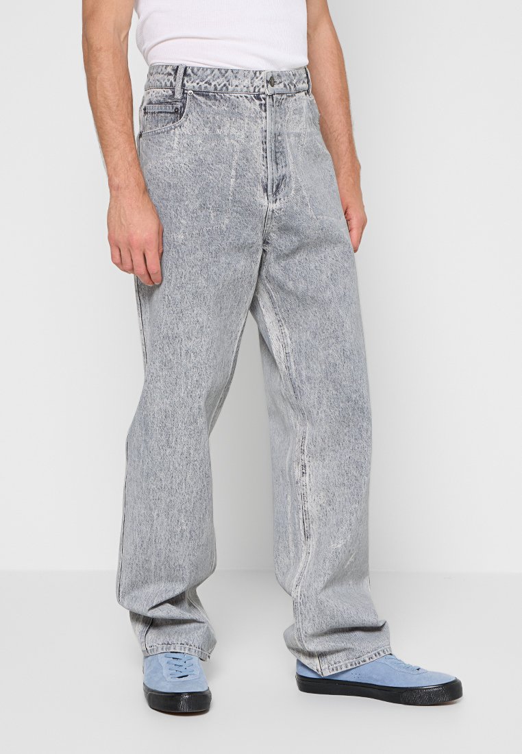 Lichtgrijze denim jeans met een ontspannen pasvorm, voorzien van een vervaagde was, een vijf-pocket ontwerp en subtiele stikdetails. Gepaard met blauwe schoenen.
