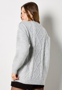 Jasnoszary sweter z dzianiny w warkocze, z teksturowanym wzorem w diamenty, ściągaczami przy mankietach i okrągłym dekoltem.