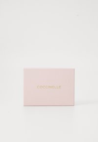 Růžová obdélníková krabice s hladkým povrchem, na přední straně se zlatým nápisem "COCCINELLE". Minimalistický design bez dalších detailů.