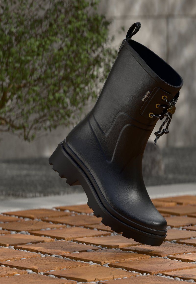 Schwarzer Regenstiefel bis zum Knöchel mit dicker Profilsohle und Schnürdetails, schwebend über braunen Holzklötzen mit kleinen grauen Steinen.