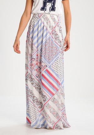 Vrouw draagt een lange patchworkrok met bloemmotieven, sterren en strepen in blauw, rood, wit en zwart.