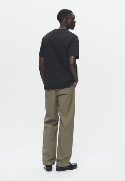 Tricou negru cu mânecă scurtă asortat cu pantaloni kaki. Tricoul are un croi clasic; pantalonii sunt dintre cei cu o potrivire lejeră, cu o textură netedă și picior drept.