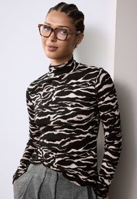 Haut à col roulé côtelé noir et rose avec un motif zèbre, associé à un pantalon gris texturé taille haute. Lunettes à monture transparente portées.