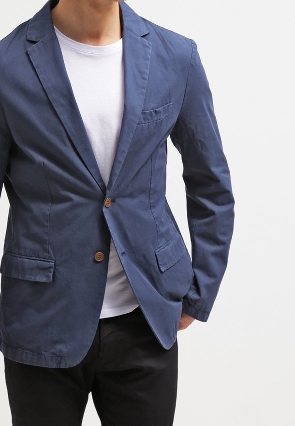 Námořnický modrý blazer vyrobený z lehkého materiálu, zapínání na jediné knoflíky s dvěma knoflíky, dvě přední kapsy a elegantní design. Nosený přes bílé tričko.