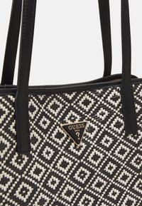 Sac fourre-tout noir et blanc à motif avec un design tissé texturé, doté de poignées en synthétique noir et d'une plaque logo dorée.