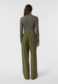Obcisły, zielony golf w paski, zestawiony z oliwkowymi, szerokimi spodniami o wysokim stanie, wyposażonymi w dwie kieszenie z tyłu.