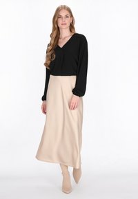Top nero a maniche lunghe con scollatura a V, abbinato a una gonna lunga beige fluidamente. Presenta una leggera texture e stivali aderenti alla caviglia.