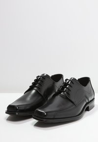 Chaussures habillées en cuir noir avec un bout arrondi, un laçage à cinq œillets et un subtil détail de couture sur les côtés.