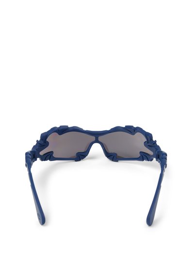 Blaue Sonnenbrille mit gezackten, unregelmäßigen Rahmen und dunkel getönten Gläsern, von vorne auf weißem Hintergrund gezeigt.