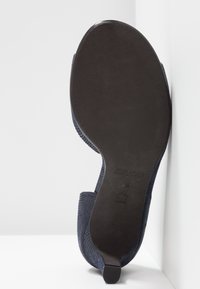 Chaussure bleu marine avec un dessus en tissu tressé et une semelle en caoutchouc noir lisse. La chaussure présente un talon effilé et une discrète empreinte de logo.