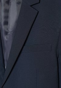 Σκούρο μπλε σκούρο σακάκι με ύφασμα ομαλής υφής, πέτα με εγκοπή και μία τσέπη στο στήθος. Η εσωτερική επένδυση έχει σατέν φινίρισμα.