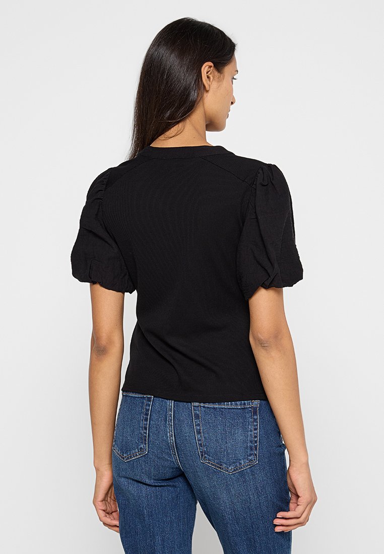 Top negro de canalé con mangas abullonadas, diseño ajustado y escote redondo, combinado con pantalones vaqueros de tiro alto azules.