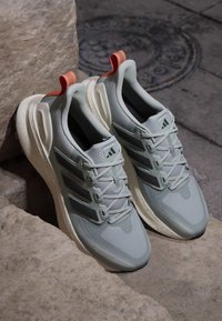 Par lysegrå Adidas løbesko med orange trækkebånd og plettede hvide mellemsåler, der hviler på stentrapper.