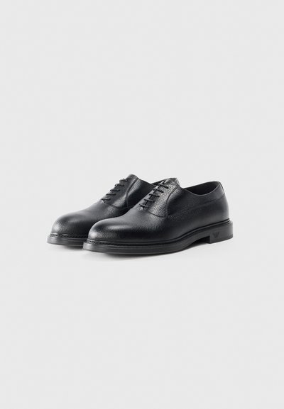 Black leather shoes featuring a smooth texture, rounded toe, lace-up design, and a flat rubber sole with a subtle logo accent.