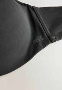 Zwarte bh van gladde stof, met onderwire ondersteuning en een klein geprint logo "self." bij de sluiting. Naadloos ontwerp met verstelbare bandjes.