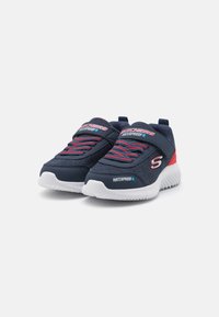 Baskets imperméables navy avec tige en tissu texturé, accents rouges contrastants, lacets élastiques et semelle en caoutchouc blanc.
