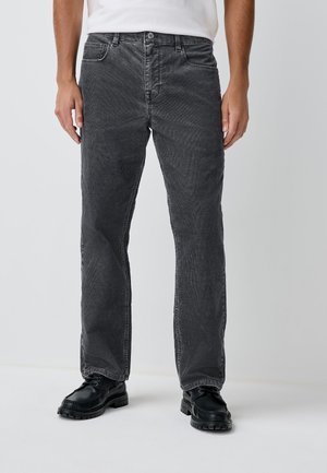 Schwarze Cordhosen mit geradem Bein, ausgestattet mit Fronttaschen, einem Knopfverschluss und feiner Textur. Dazu schwarze Schuhe.