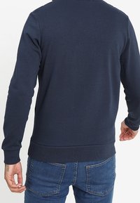 Námořnická modrá mikina vyrobená z měkké látky, s dlouhými rukávy, žebrovanými manžetami a kulatým výstřihem, s jednoduchým zadním pohledem.